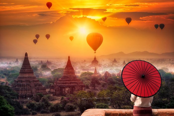 Unidentified Burmese woman holding traditional red umbrella and looks at Hot air balloon over plain of Bagan in misty morning, Mandalay, Myanmar