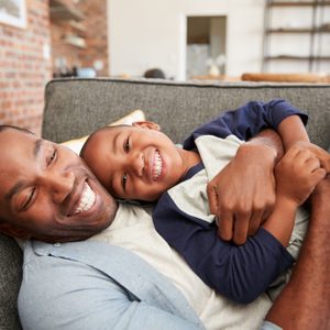 Father And Son Cuddling On Sofa Together