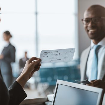 close-up shot of smiling african american businessman giving passport to staff at airport check in counter