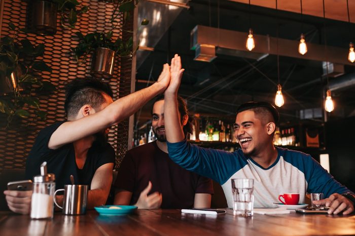 Happy arabic young man giving high five to his friend. Group of mixed race people having fun in lounge bar