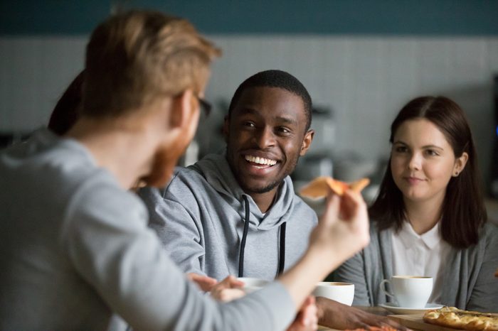 Happy millennial african american man laughing at joke hanging in pizzeria sharing pizza with best friends, smiling attractive black guy having fun talking to buddy sharing lunch at cafe restaurant