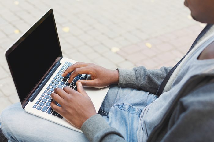 Male hands typing on laptop closeup. Black man working outdoors on computer with blank screen for copy space. Technology, communication, education and remote working concept.