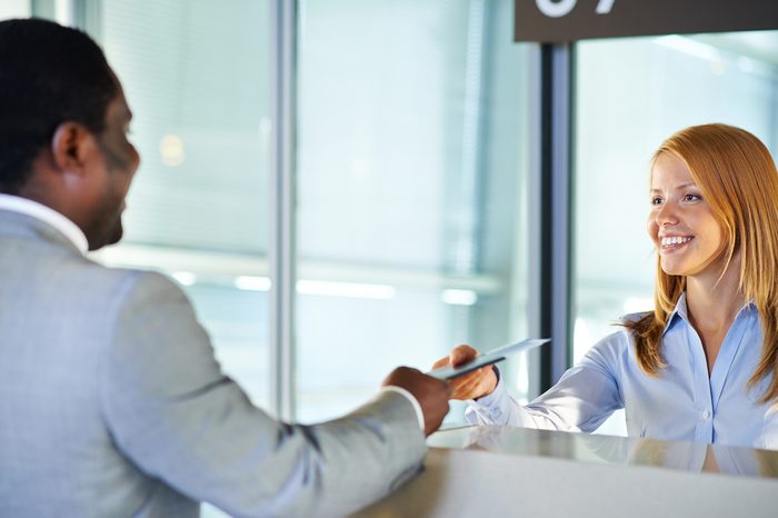 Friendly woman giving passport and ticket back to businessman at airport check-in counter