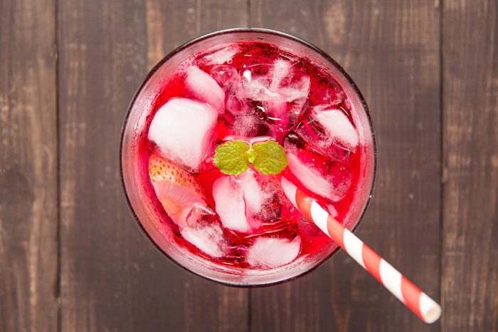 Red Cocktail with mint and ice on wooden table.