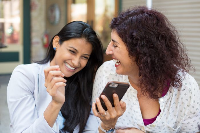 Closeup portrait two surprised girls looking at cell phone, discussing latest gossip news, sharing intimate moments, shopping, laughing at what they see, isolated outdoors background