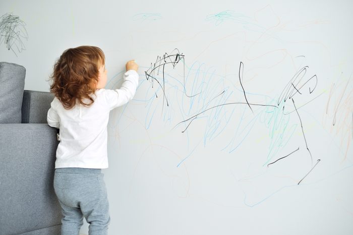 Curly cute little baby girl drawing with crayon color on the wall. Works of child