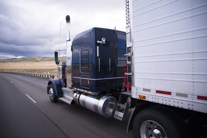 Classic bonneted American semi truck with chrome trim and a refrigerator trailer drive on the straight road in the California fields.