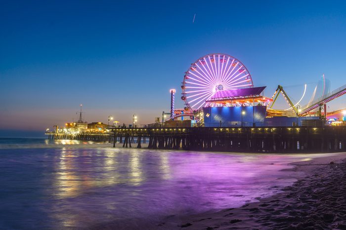 Santa Monica Pier illuminated with new LED lights at night with a reflection that can be seen on the waves.