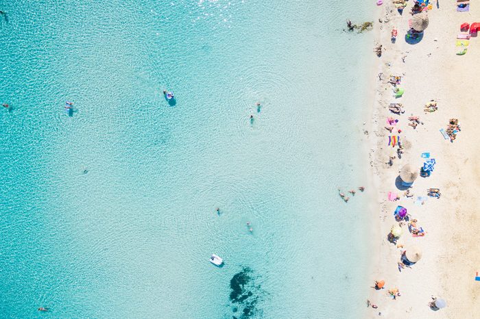 Aerial view of sandy beach with tourists swimming in beautiful clear sea water