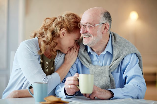 Portrait of smiling senior couple sitting close together cuddling caringly and laughingat kitchen table  with tea cups and homemade cookies