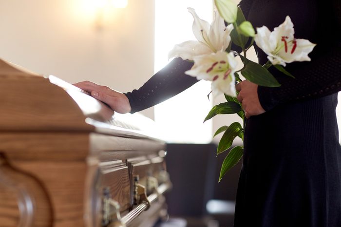 people and mourning concept - woman with white lily flowers and coffin at funeral in church