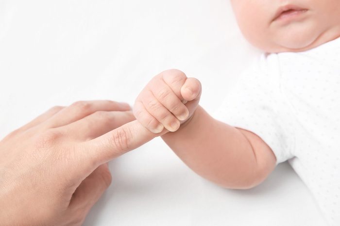 Cute little baby holding mother's finger on white background