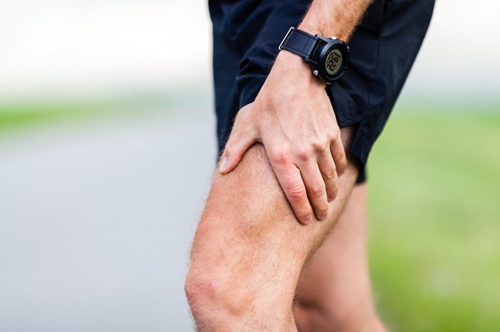 Runner leg and muscle pain during running training outdoors in summer nature. Health and fitness concept. Injured male jogger massage sore leg.