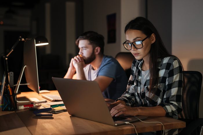 Image of two business people working with laptop and computer late at night in their office.