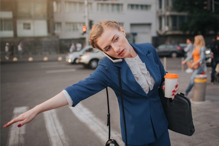 oung stylish businesswoman with coffee cup catching a taxi. Woman doing multiple tasks. Multitasking business woman.