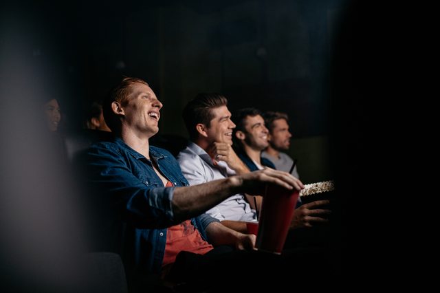 Group of friends sitting in multiplex movie theater. Young people watching movie in cinema hall and smiling.