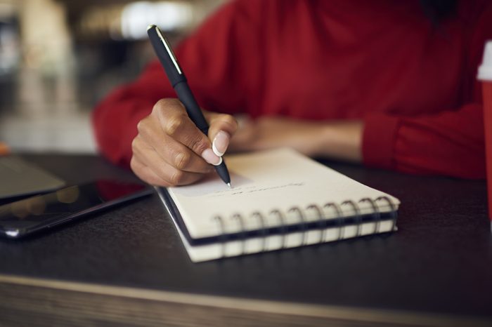 Selective focus on handwriting in spiral notebook creating to do list with targets on white page, cropped image of afro american female designer drawing sketches for project in diary with pen