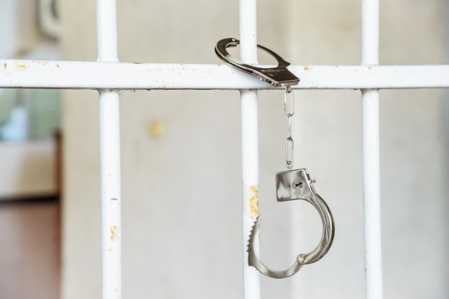 Closeup of unlocked handcuffs hanging on jail bars