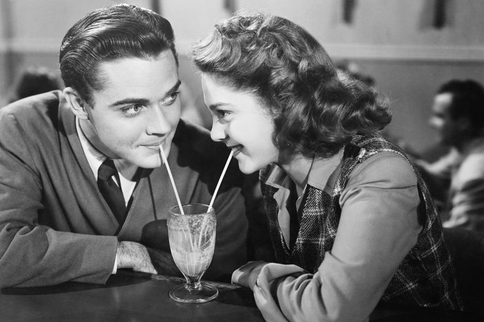 Couple in a restaurant looking at each other and sharing a milk shake with two straws