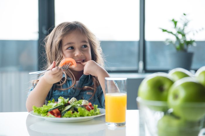 Portrait of cheerful asian girl eating salad with joy. She is looking aside with curiosity and smiling