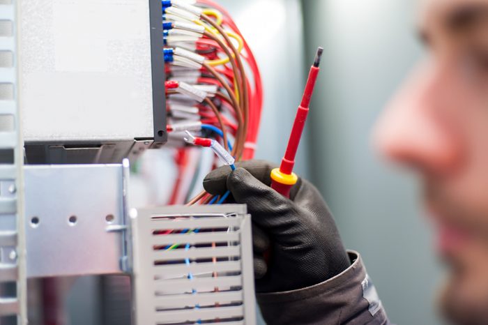 Closeup of electrician engineer works with electric cable wires of fuse switch box. Electrical equipment