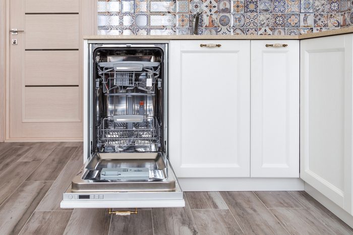 Build-in dishwasher with opened door in a white kitchen in neoclassical style with wooden front