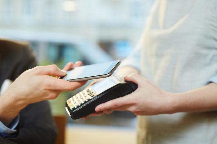 Close-up view of unrecognizable waitress holding terminal and male guest paying for meal with modern smartphone