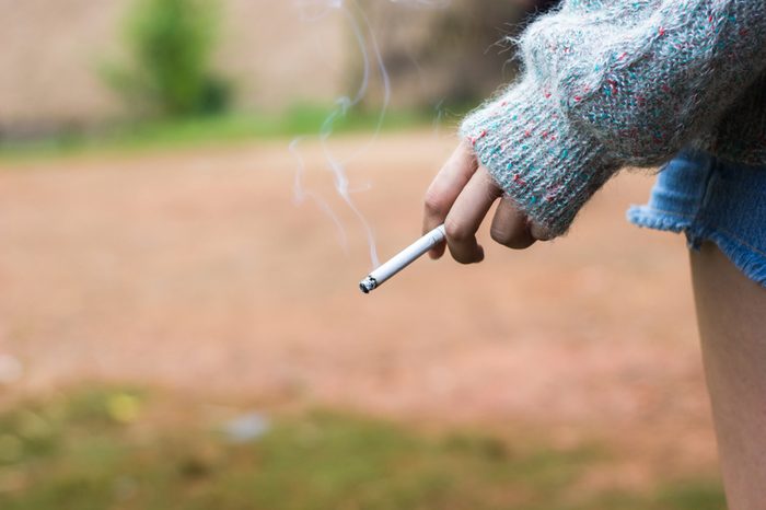 Female hand holding cigarette with smoke and copy space. Photo for learn about the dangers of cigarettes.