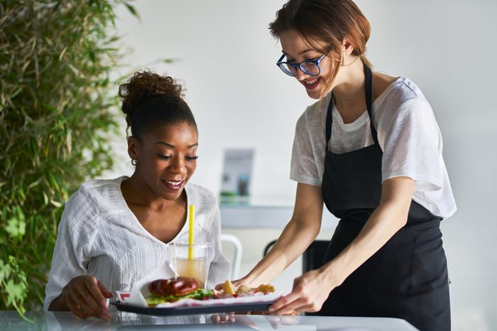 african american women being served tray of healthy vegan food at restaurant