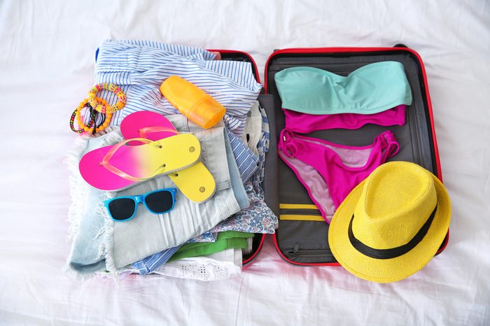 Open suitcase with different clothes and accessories for summer journey on bed