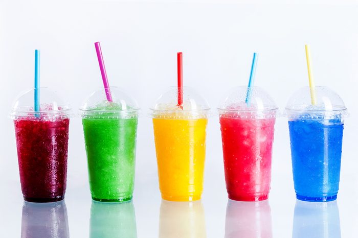 Panoramic Still Life of Colorful Frozen Fruit Slush Granita Drinks in Plastic Take-Away Cups with Lids and Drinking Straws in front of White Background