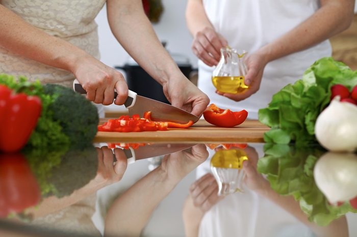 Close-up of human hands cooking in a kitchen. Friends having fun while preparing fresh salad. Vegetarian, healthy meal and friendship concept