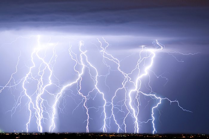 Massive colorful cloud to ground crazy skies lightning bolts hitting the horizon of city lights.