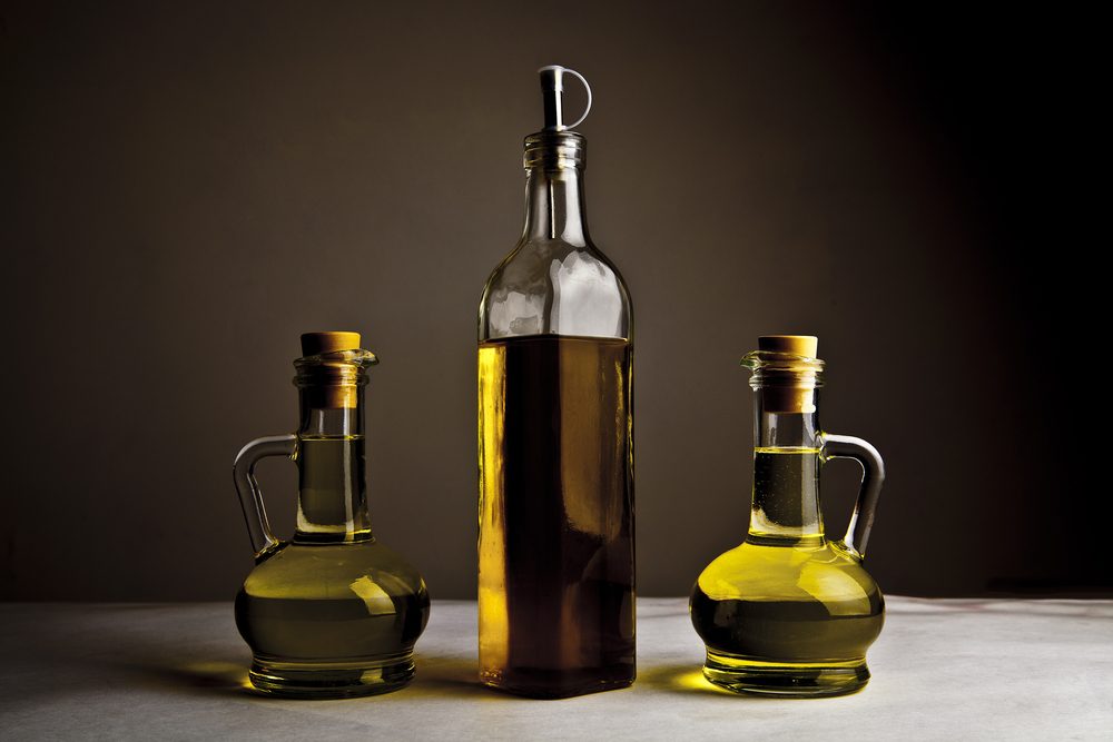 Backdrop of three olive oil glass transparent bottle with cork stand on white table on kitchen space room, on dark black background Empty space for inscription