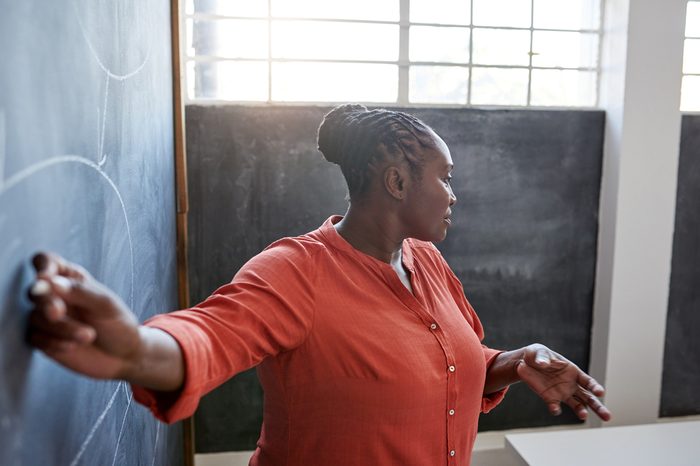 Focused and confident young African businesswoman giving a presentation to unseen colleagues while writing on a chalkboard in a modern office