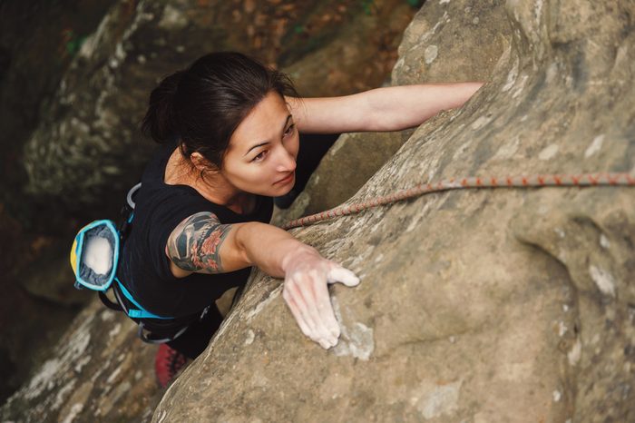 Beautiful young woman climbing on rock outdoor in summer, top view