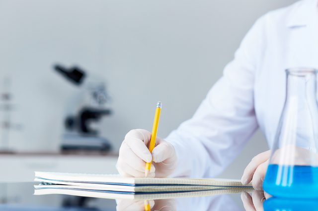 Hand of chemist with pencil writing down observations in laboratory