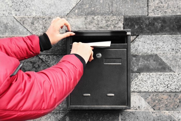 Woman putting envelope into mailbox on wall of building outdoors