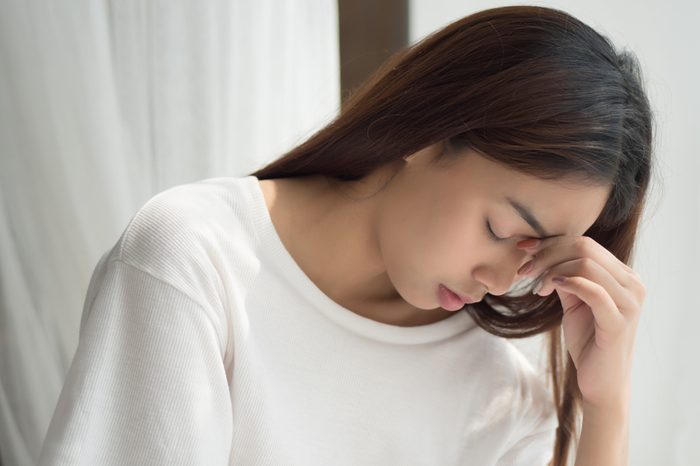 portrait of stressed sick woman with headache; depressed woman suffers from vertigo, dizziness, migraine, hangover; health care concept; 20s young adult asian middle east, mixed race woman model