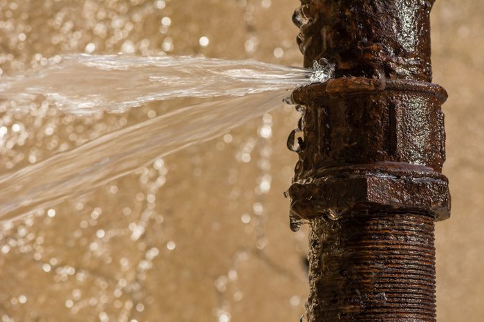 Rusty burst pipe spraying water after freezing in winter.