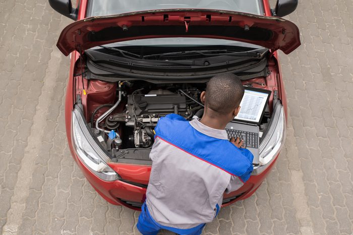 Young Male Mechanic Using Laptop While Examining Car Engine