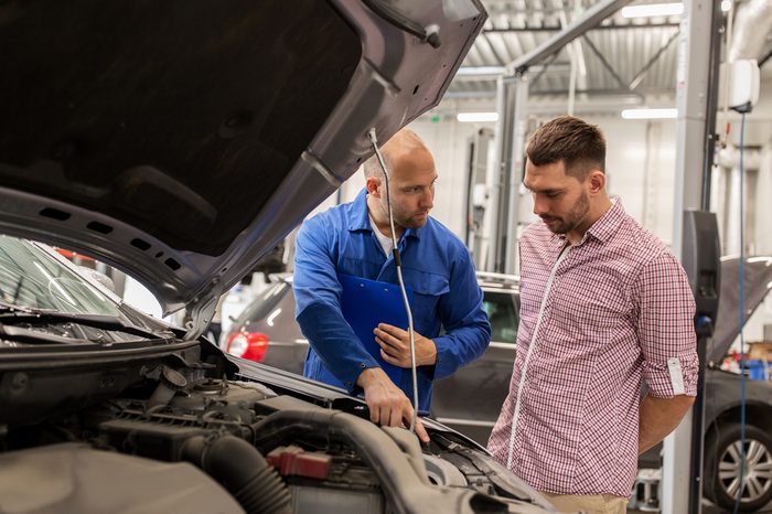 auto service, repair, maintenance and people concept - mechanic with clipboard talking to man or owner at car shop