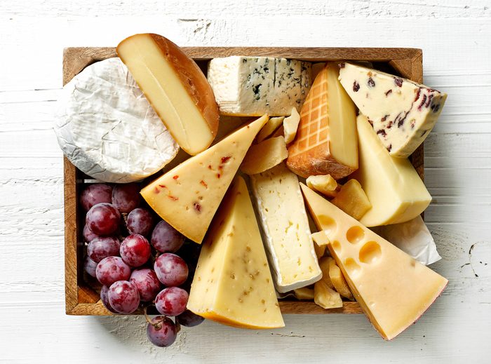 various types of cheese in wooden box on white wooden table, top view