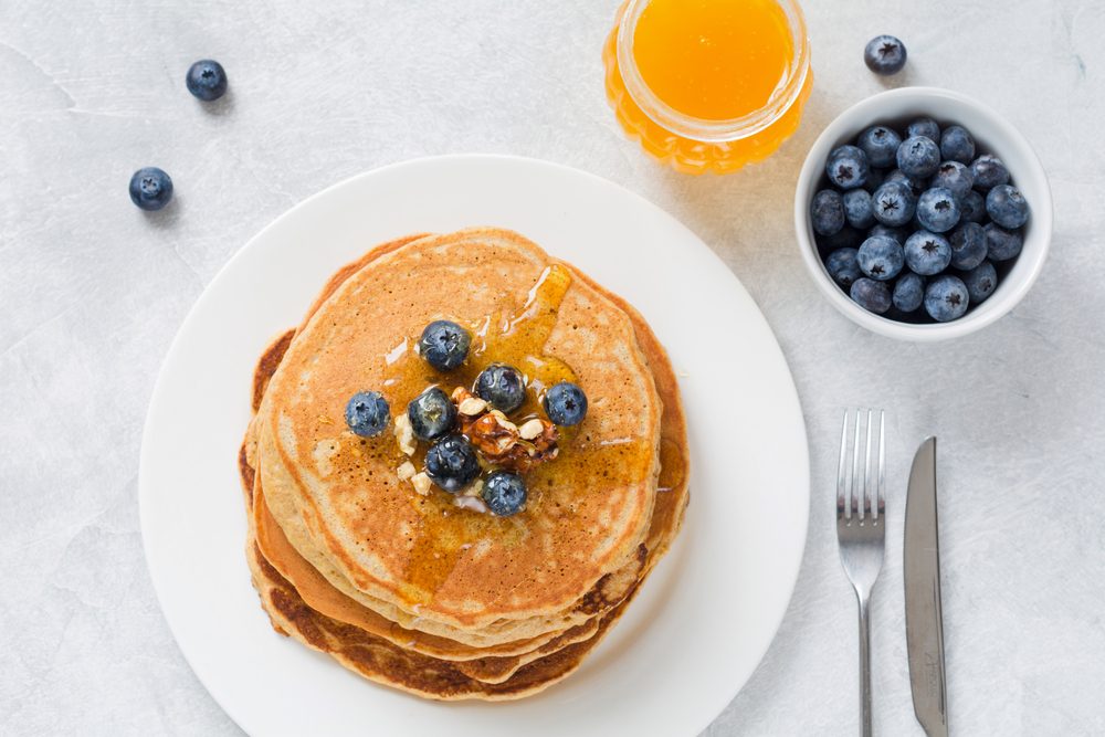 Stack of pancakes with fresh blueberries, nuts and honey on white plate. Healthy breakfast food. Table top view.