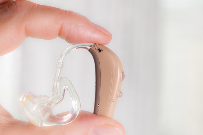 Closeup senior woman with electronic hearing aid in her hand. Health care, hear disorder, device for the deaf.