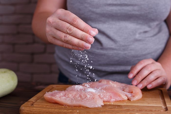 Overweight woman hands adding salt to raw chicken breasts. Dieting, healthy low calorie food, weight losing concept