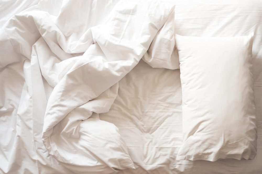 Messy bed. White pillow with blanket on bed unmade. Concept of relaxing after morning. With lighting window. Top view. 