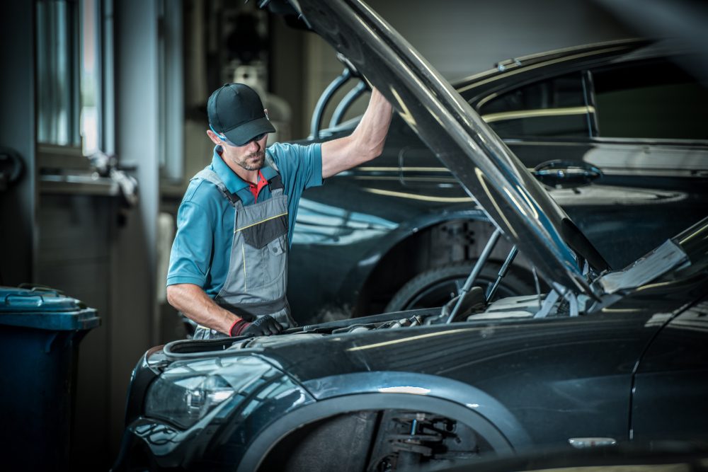 Car Mechanic and His Job. Caucasian Auto Service Worker in Front of Broken Vehicle.