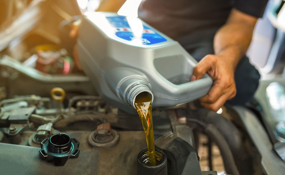 Car mechanic replacing and pouring fresh oil into engine at maintenance repair service station.