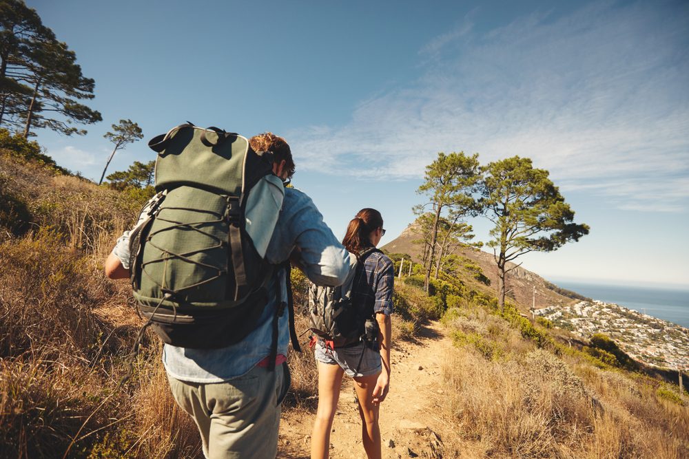 Rear view of two young people walking down the trail path on mountain. Young couple hiking with backpacks.